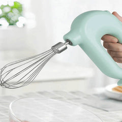 Electric Hand Mixer - Hand holding the mint green unit with whisk attachment positioned over a clear glass mixing bowl