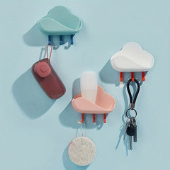 Cloud Wall Hooks - Teal, pink, and white adhesive storage units mounted on a light blue wall, holding small items with keys and a bath sponge hanging from pegs