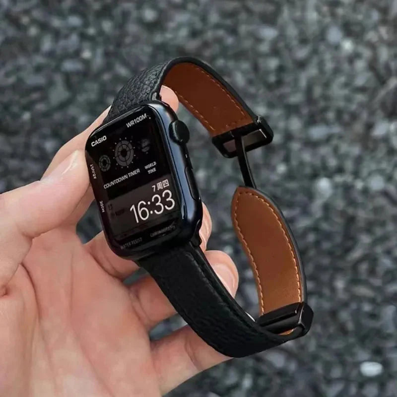 Apple Watch Band - Hand holds a smartwatch with black pebbled leather band, watch face shows Casio branding and 16:33 time