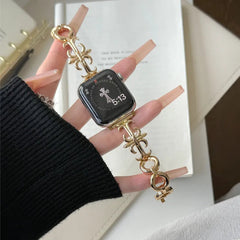 Hand with long manicured nails holding a gold-toned decorative apple watch band attached to a smartwatch