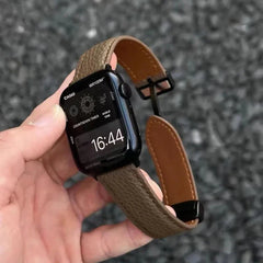 Apple Watch Band - taupe pebbled leather strap with tan lining held in hand against gravel background