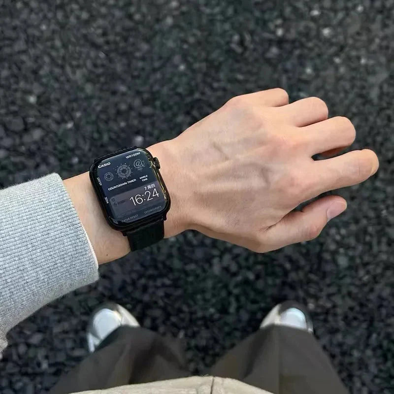 Apple Watch Band - black pebbled leather strap worn on wrist over gravel ground