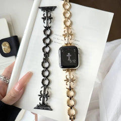 Two cross-style chain apple watch bands displayed on an open book, one installed on an Apple Watch showing 5:12.