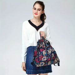 Travel Backpack - Young woman holding a floral print drawstring backpack, wearing a white v-neck sweater and denim mini skirt