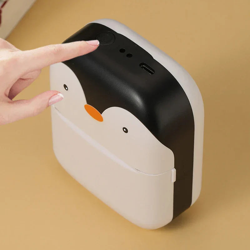 Impresora térmica de bolsillo - Mano presionando el botón de encendido en la parte superior de una mini impresora con forma de pingüino