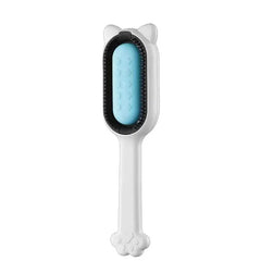 White handheld pet grooming brush with cat ear top, light blue cleaning insert, black trim, and paw-shaped handle end.