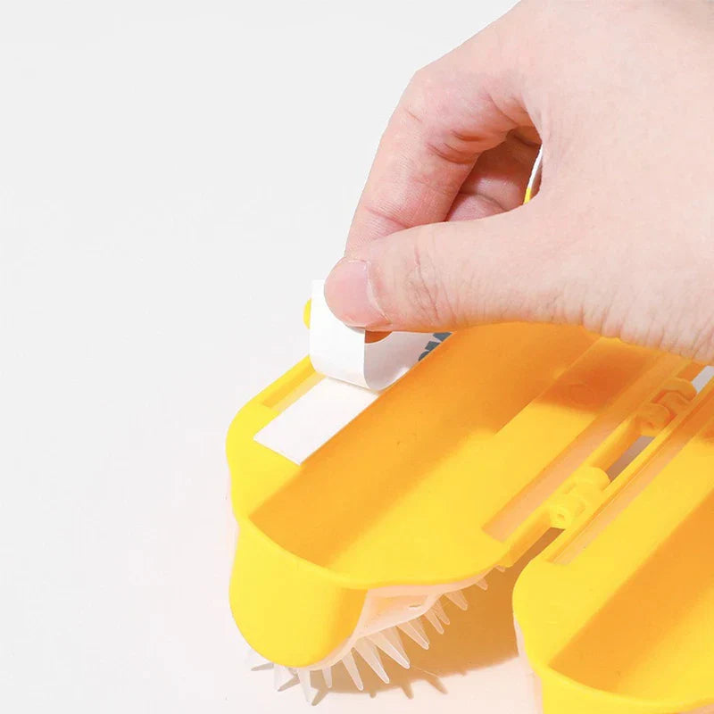 Pet Double Row Grooming Massager Brush - Hand peeling adhesive backing from a yellow dual-cylinder pet grooming tool.