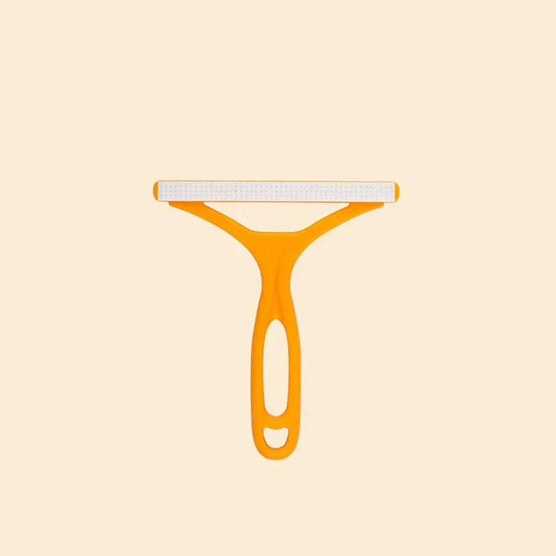 Pet Grooming Deshedding Brush - Orange T-shaped manual fabric cleaner tool with white textured cleaning head, centered on pale beige background