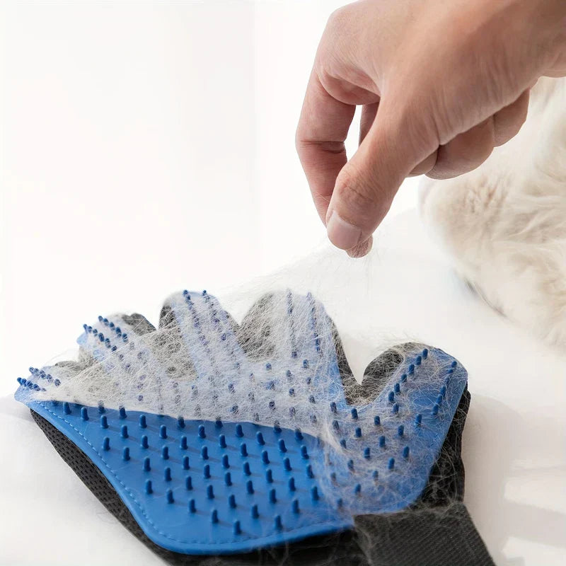 A hand lifts a tuft of white fur off a pet grooming deshedding hair remover mitt laid on a white surface.