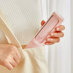 A hand tucks a closed light pink pet hair remover brush into the side pocket of a beige canvas tote bag.