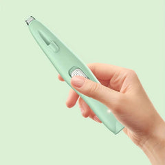 A hand holds a light green hair trimmer with a thumb on its side switch, set against a pale green background.