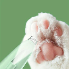 A close-up view of a light green hair trimmer positioned to trim fur between a cat's pink paw pads.