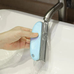 Hand holding a light blue dog grooming comb under a running faucet in a white sink, rinsing the comb's teeth