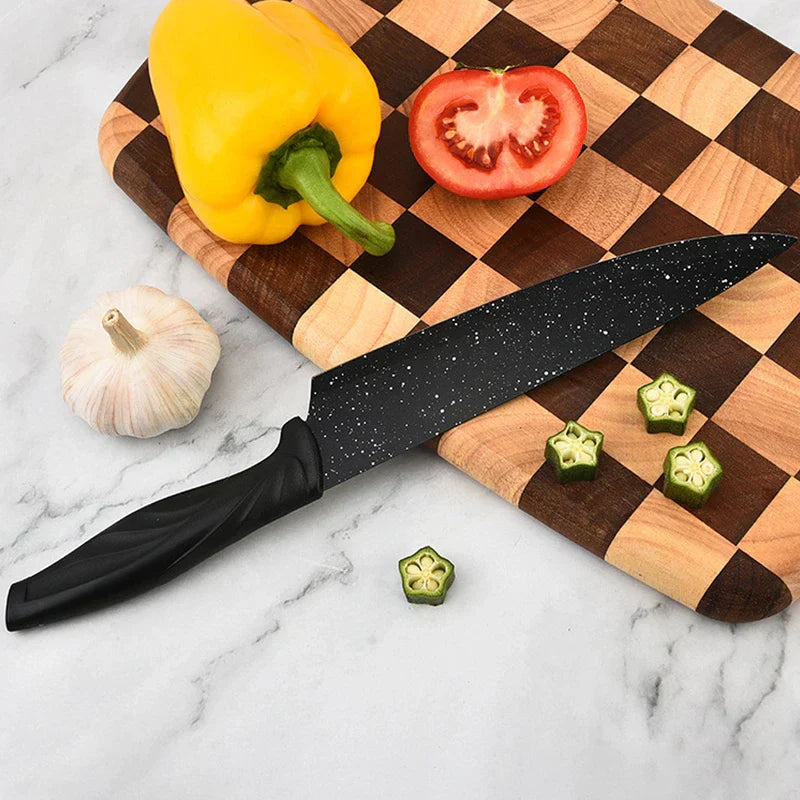 Black chef knife from a kitchen utensil set rests on checkered cutting board with yellow bell pepper, tomato, garlic, and sliced okra on marble countertop