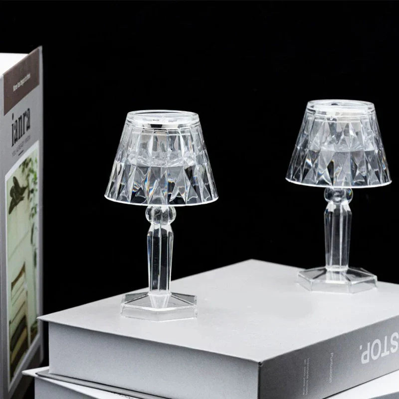 Two unlit clear faceted lamp-shaped led candle decor pieces placed on stacked light gray boxes against black background