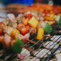 Close-up of colorful meat and vegetable skewers cooking on a grill grate over glowing charcoal