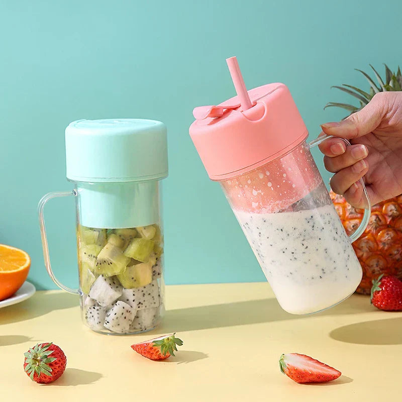 Juicer Cup - Two juicer cups on a table: mint green with cut fruit inside, pink one held by a hand with a creamy smoothie and a straw, surrounded by fresh fruit