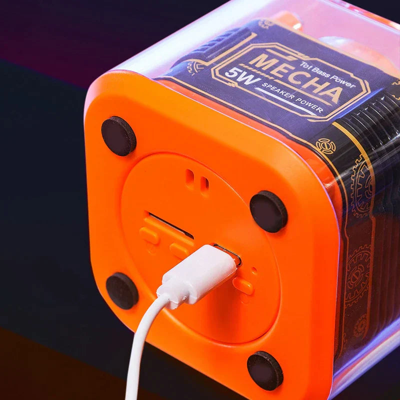 Bottom view of an orange 5W MECHA portable bluetooth speaker with a USB-C charging cable plugged in.