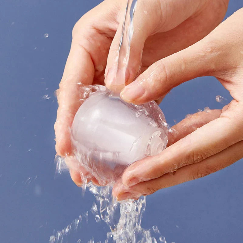 Hands washing a clear spherical lint remover roller under running water against a blue background
