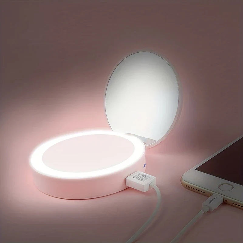 espejo de maquillaje con luz led - espejo de maquillaje rosa con luz led con cable USB conectado, junto a un teléfono inteligente cargándose sobre una superficie rosa suave