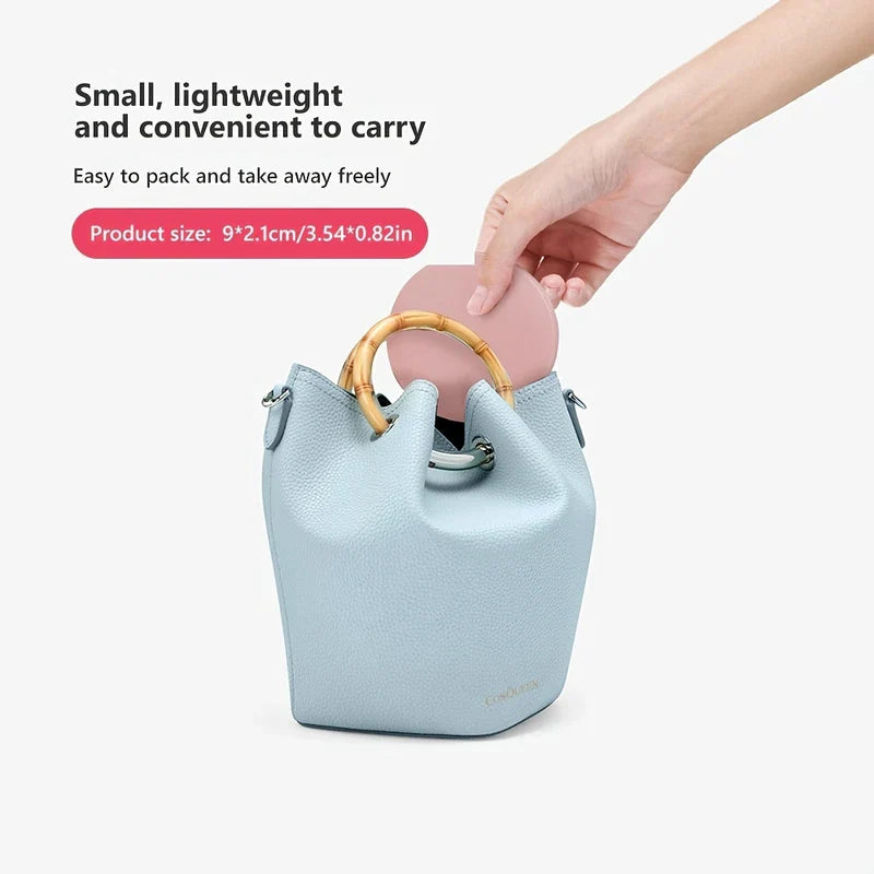 Hand placing pink round led makeup mirror into light blue mini bucket bag, with text noting its small portable size