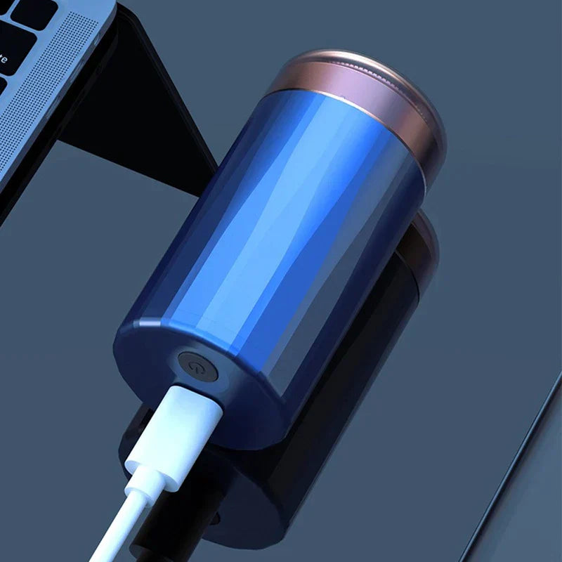 Blue mini electric shaver plugged with USB charging cable, resting on dark reflective surface near laptop.
