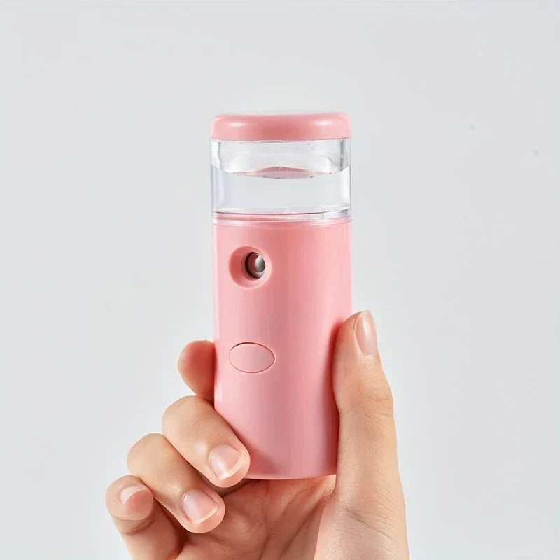 Hand holding a pink portable nano facial mist sprayer against a plain light gray background