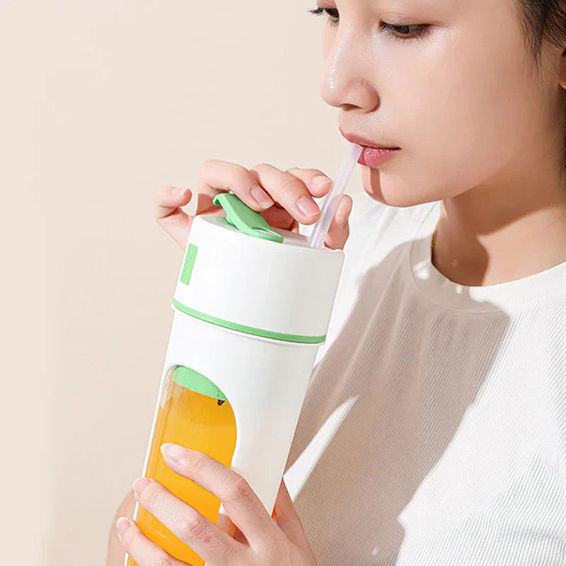 Person drinking orange juice from straw in white and green blender juicer cup with visible yellow liquid inside