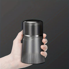 A hand holds a compact dark electric shaver with a metallic mid-band and ribbed lower section against a dark gray background