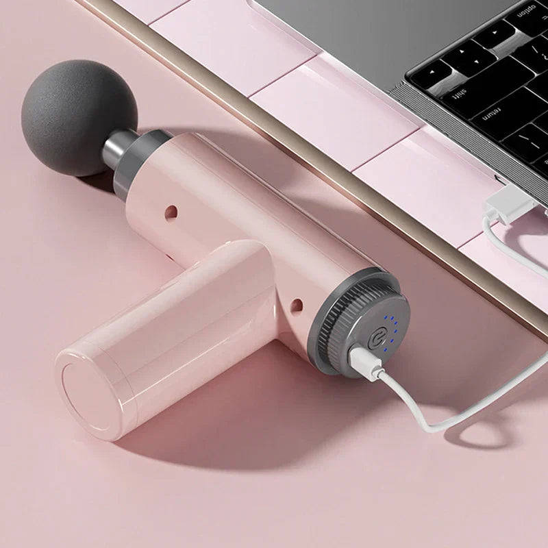 Rosa Psoas-Muskelmassagegerät mit eingestecktem USB-Ladekabel, neben einem Laptop auf rosa Unterlage liegend