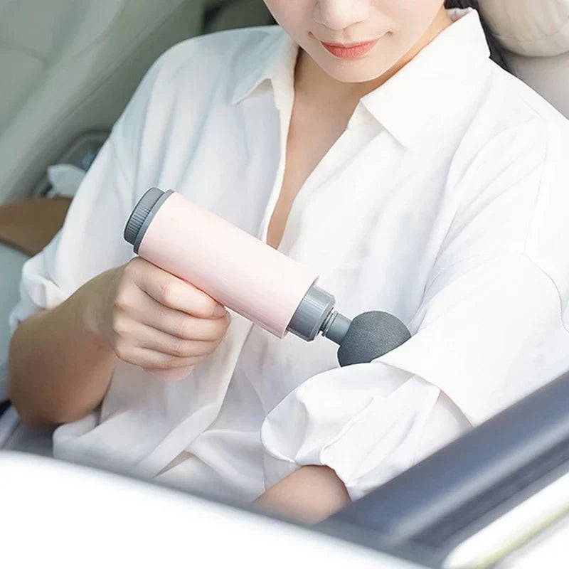 Person in white shirt using a pink psoas muscle massager on their upper arm while sitting in a car