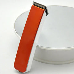 Orange and white hair clipper trimmer leaning against a white round display stand on a white surface