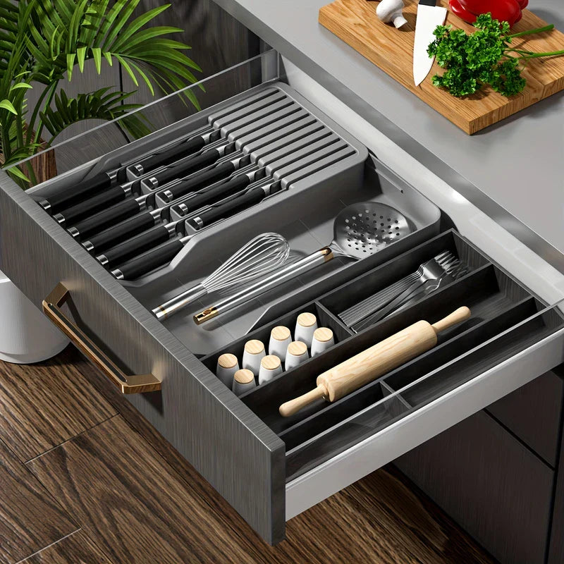 bloque de cuchillos - Cajón de cocina abierto con un organizador gris para cuchillos que sostiene cuchillos y utensilios, junto con otros organizadores de cajón.