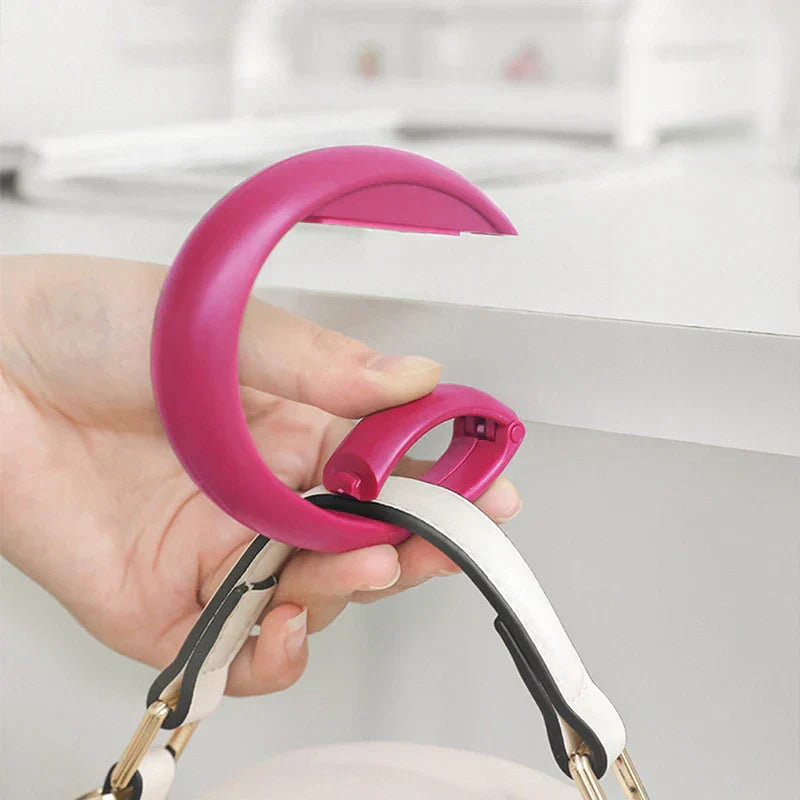 Eine Hand demonstriert einen magenta-farbenen Handtaschenhaken mit einem Taschenriemen