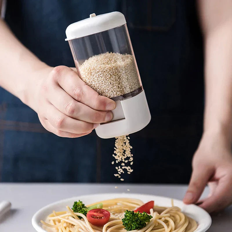Hand pressing spice dispenser to pour sesame seeds over pasta