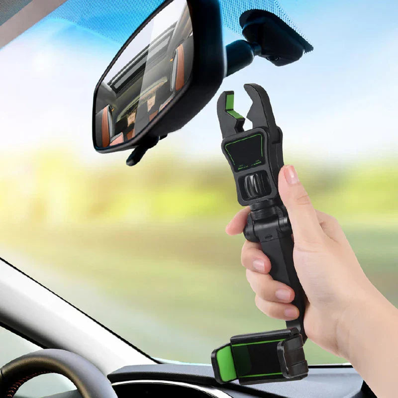 A hand holds a black and green rearview mirror phone holder near a car interior rearview mirror.