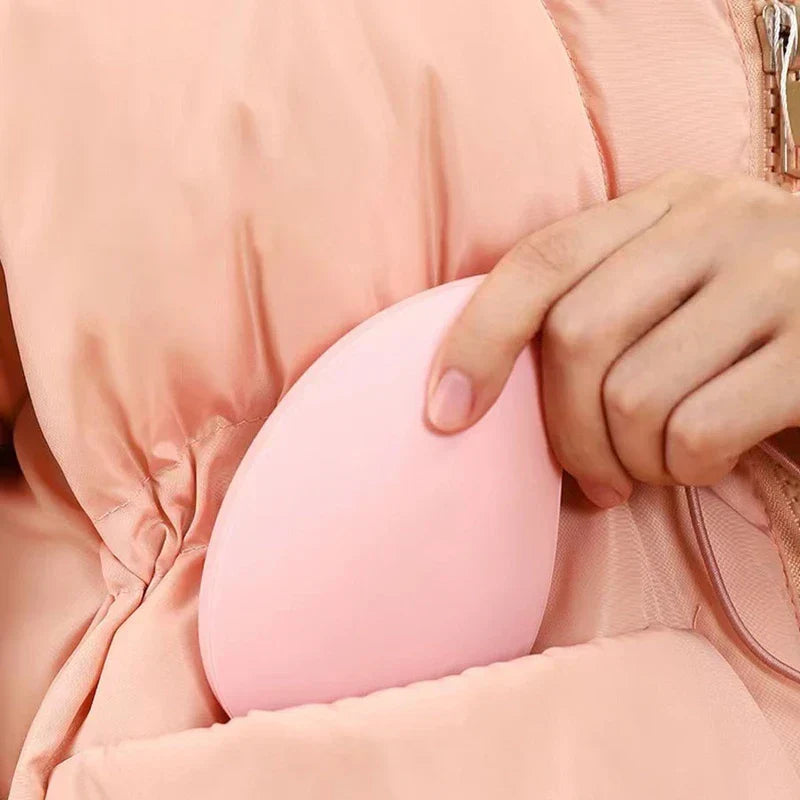 A hand holds a pink rechargeable hand warmer tucked into the pocket of a pink puffer jacket