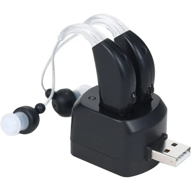 Two black rechargeable hearing aid devices plugged into a black USB charging dock with clear ear hooks and white ear tips