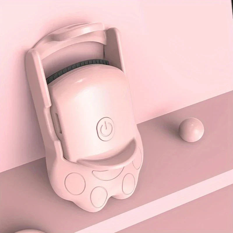 Side angled view of pink eyelash curler with cat paw design resting on a pastel pink stepped surface