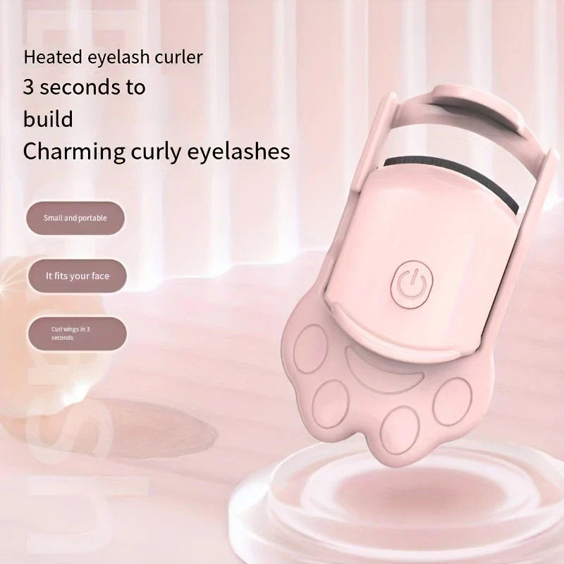 Pink heated eyelash curler with cat paw handle against soft pastel background with feature text labels