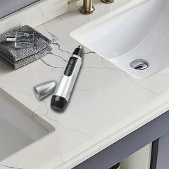 Silver nose ear hair trimmer with detached cap rests on a marble bathroom countertop near a sink and folded towels.