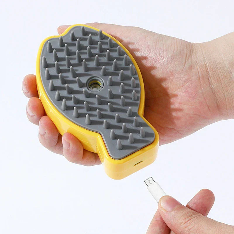 Mano sosteniendo un peine de masaje eléctrico para cuero cabelludo amarillo y gris con cable de carga USB cerca