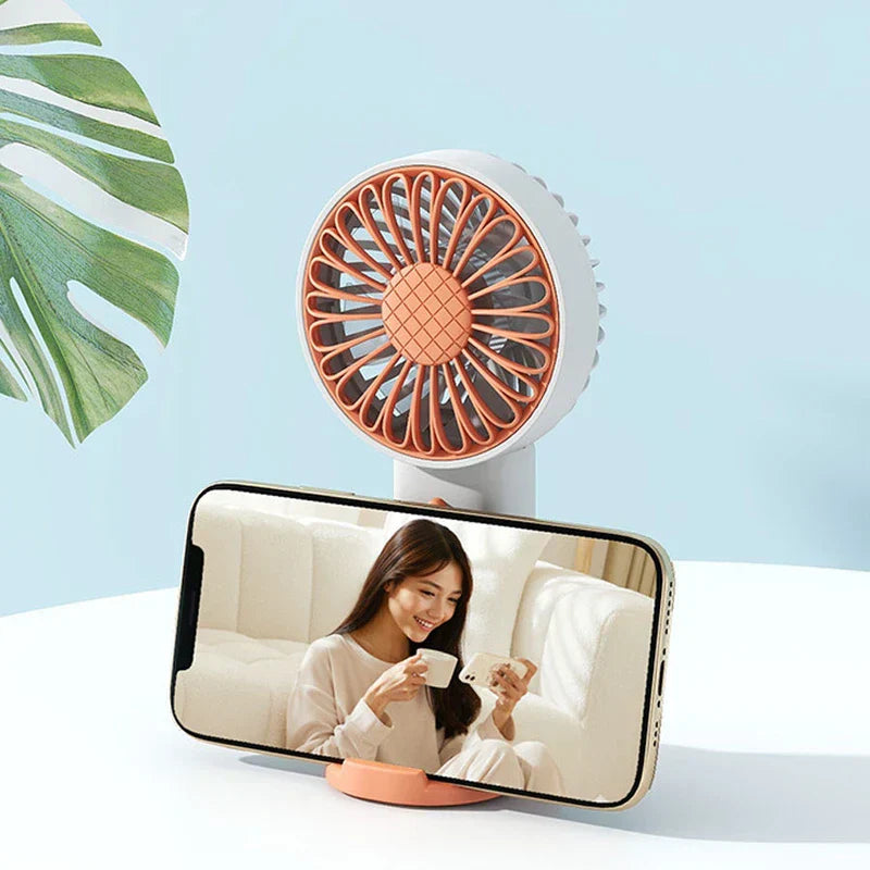 White and orange travel fan placed on a table, with its base holding a horizontal smartphone
