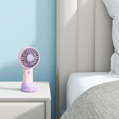 ventilador de viaje - Ventilador de viaje rosa y morado sobre una mesita de noche blanca junto a una cama con pared azul claro detrás