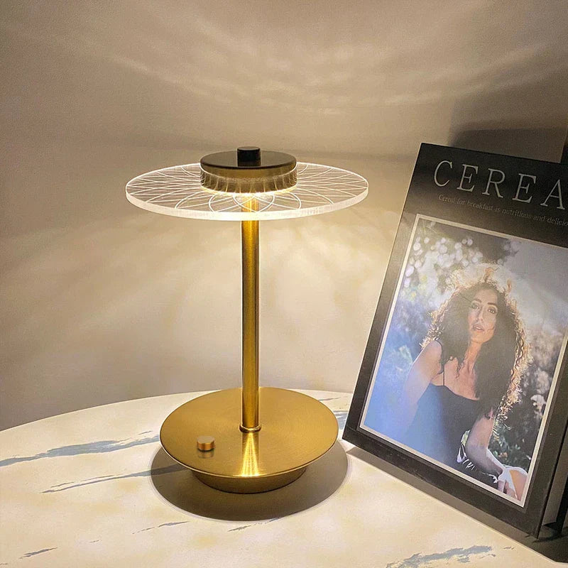 Lámpara dorada con disco circular estampado y bombillas led sobre una mesa de mármol junto a una impresión CEREA enmarcada