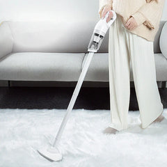 Person using a handheld vacuum with an extended wand on a white furry rug in front of a gray sofa