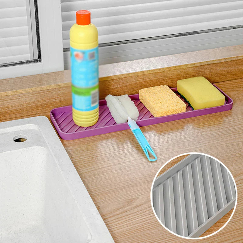 Lila Getränkematte auf Küchentheke hält eine gelbe Flasche, Reinigungsbürste und zwei Schwämme in der Nähe einer Spüle, mit eingesetztem grauem Mattendetail