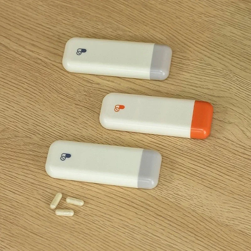 Weekly Pill Organizer - Three weekly pill organizers and three capsule pills on a light wood surface, two with gray ends, one with an orange end