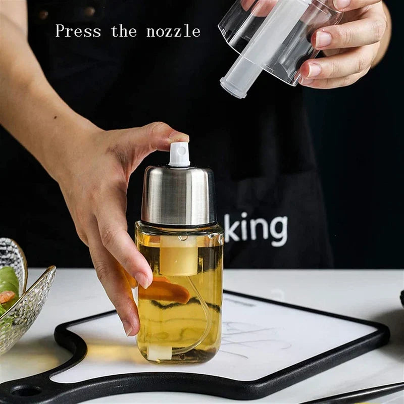 Hand presses the nozzle of a glass oil sprayer dispenser, while another hand holds its removed clear dust cap