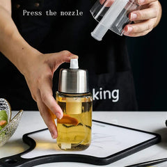 Hand presses the nozzle of a glass oil sprayer dispenser, while another hand holds its removed clear dust cap